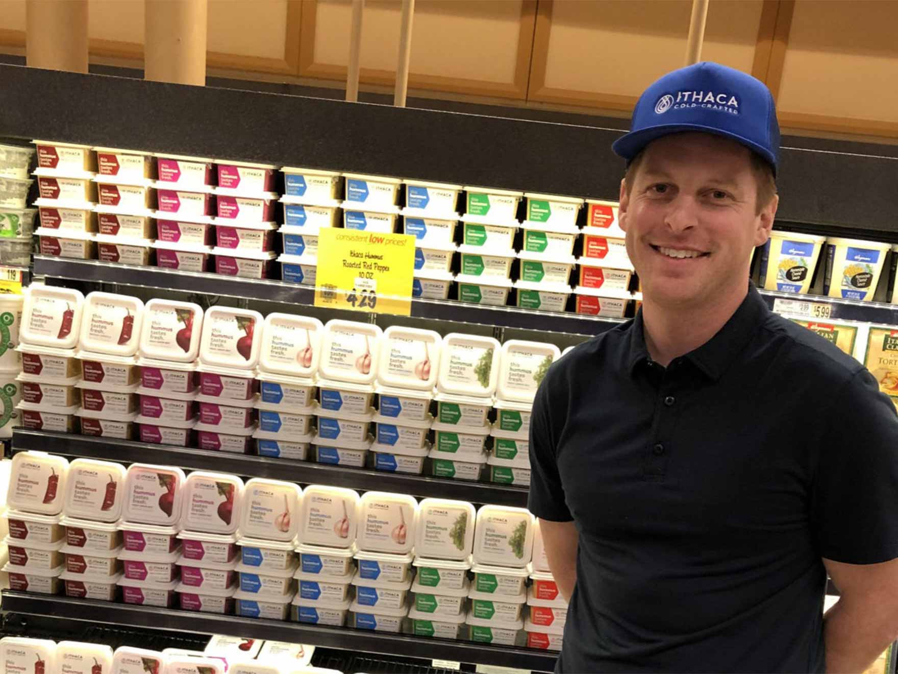 Chris Kirby '15 stands in front of a Ithaca Hummus display in a grocery store.