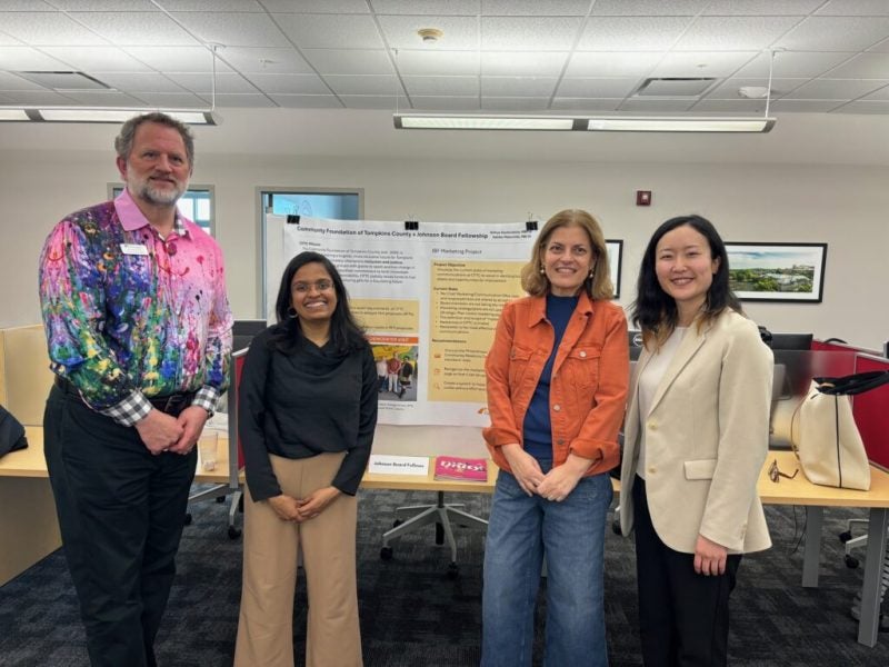 Members of the Johnson Board Fellows associated with the Cornell MBA program pose in front of a presentation poster board in an office space