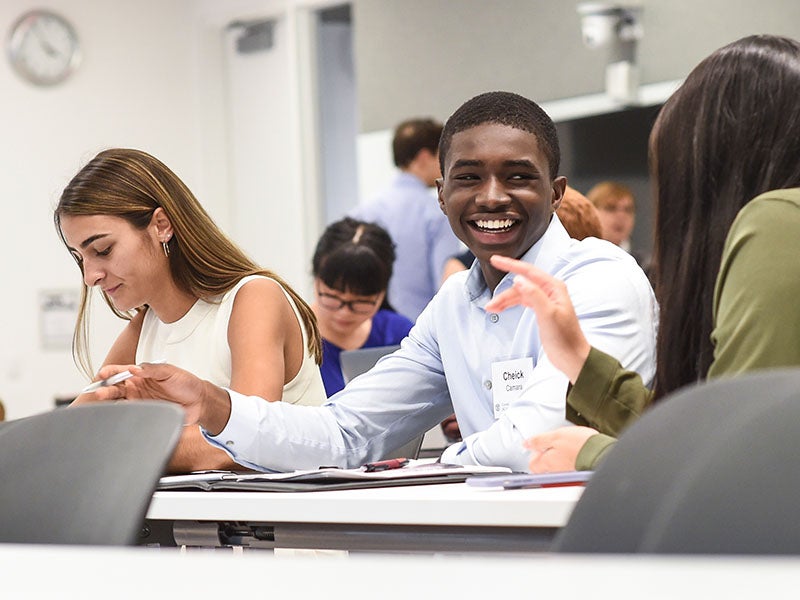 Students talking and smiling while sitting in a classroom.