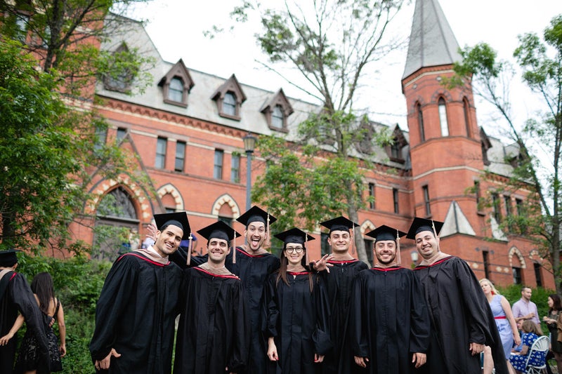 students standing in a group in graduation caps in front of an educational building