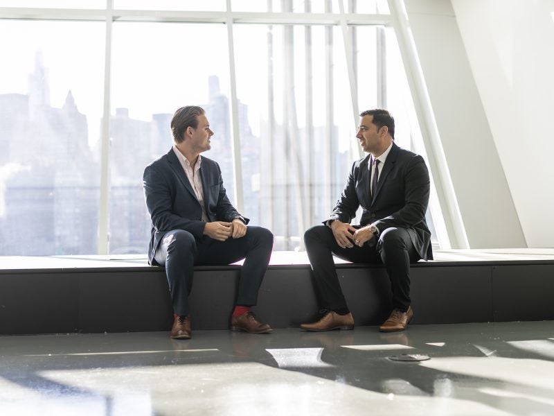 two men sitting on a bench in a building overlooking the city skyline.