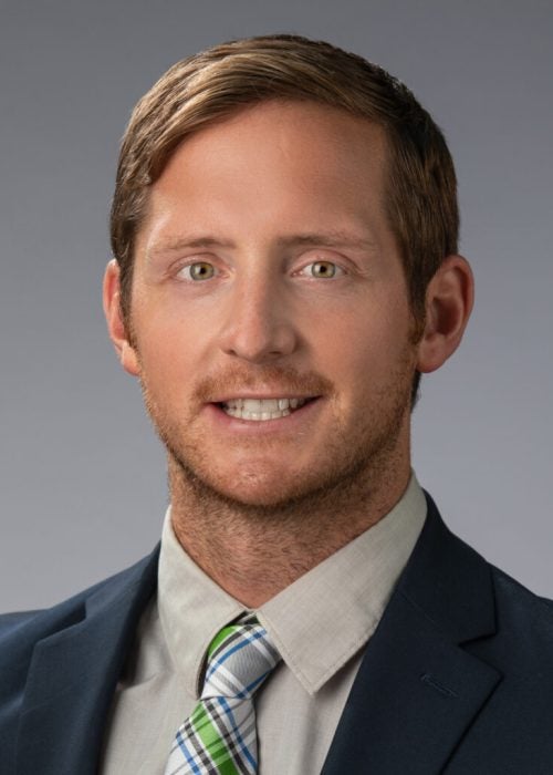Business headshot photo of a young man dressed in business formal attire against a gray backdrop