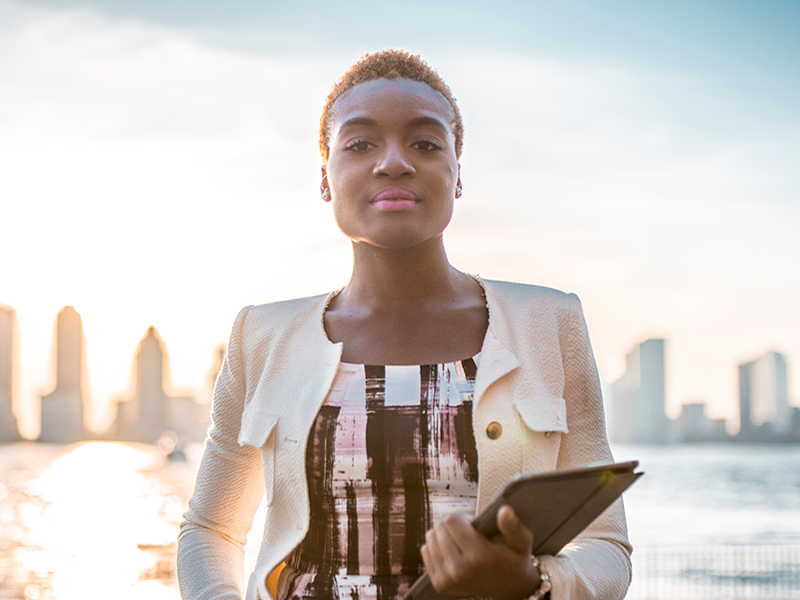 woman standing in front of river in nyc with skyline in the background