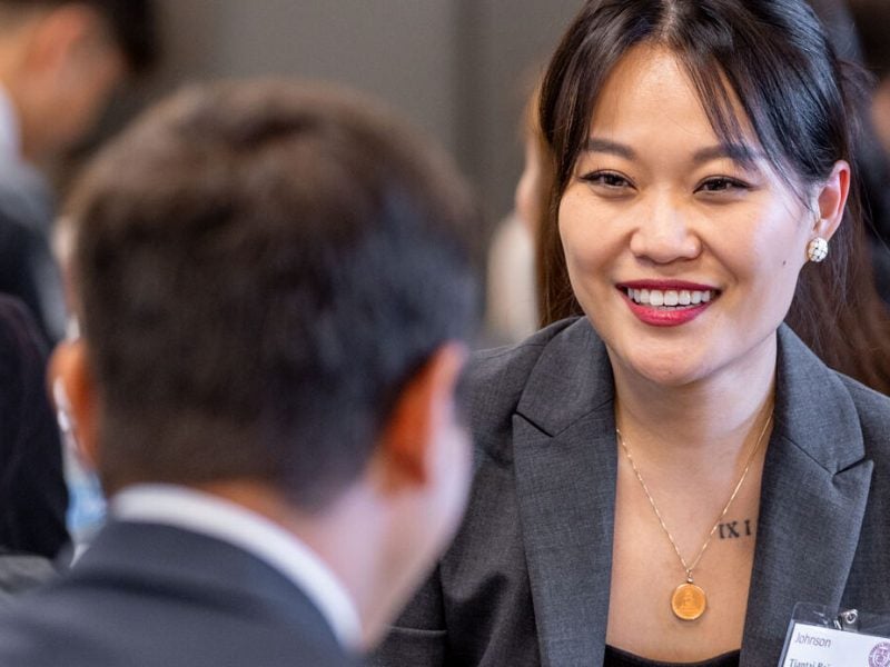 A young woman in business attire smiles in conversation with fellow students as part of the Cornell MBA program