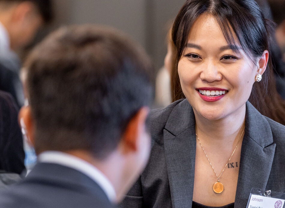 A young woman in business attire smiles in conversation with fellow students as part of the Cornell MBA program
