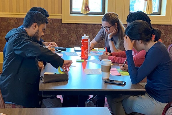 Two young men and three young women in casual attire work on a group project at a table as part of their Cornell MBA coursework