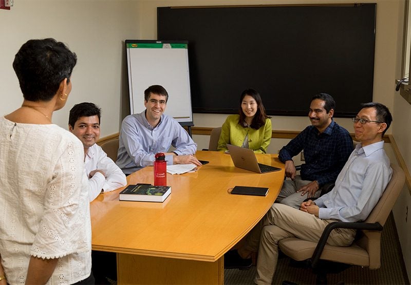 PhD student and four Johnson faculty sit around table while they listen to Nicholas H. Noyes Professor of Management, Vrinda Kadiyali.
