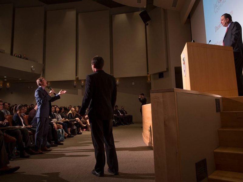 Person in an auditorium speaking to a person standing behind a podium.