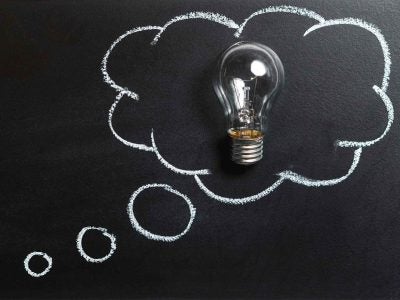 A lightbulb sits inside of a thought bubble drawn in chalk.