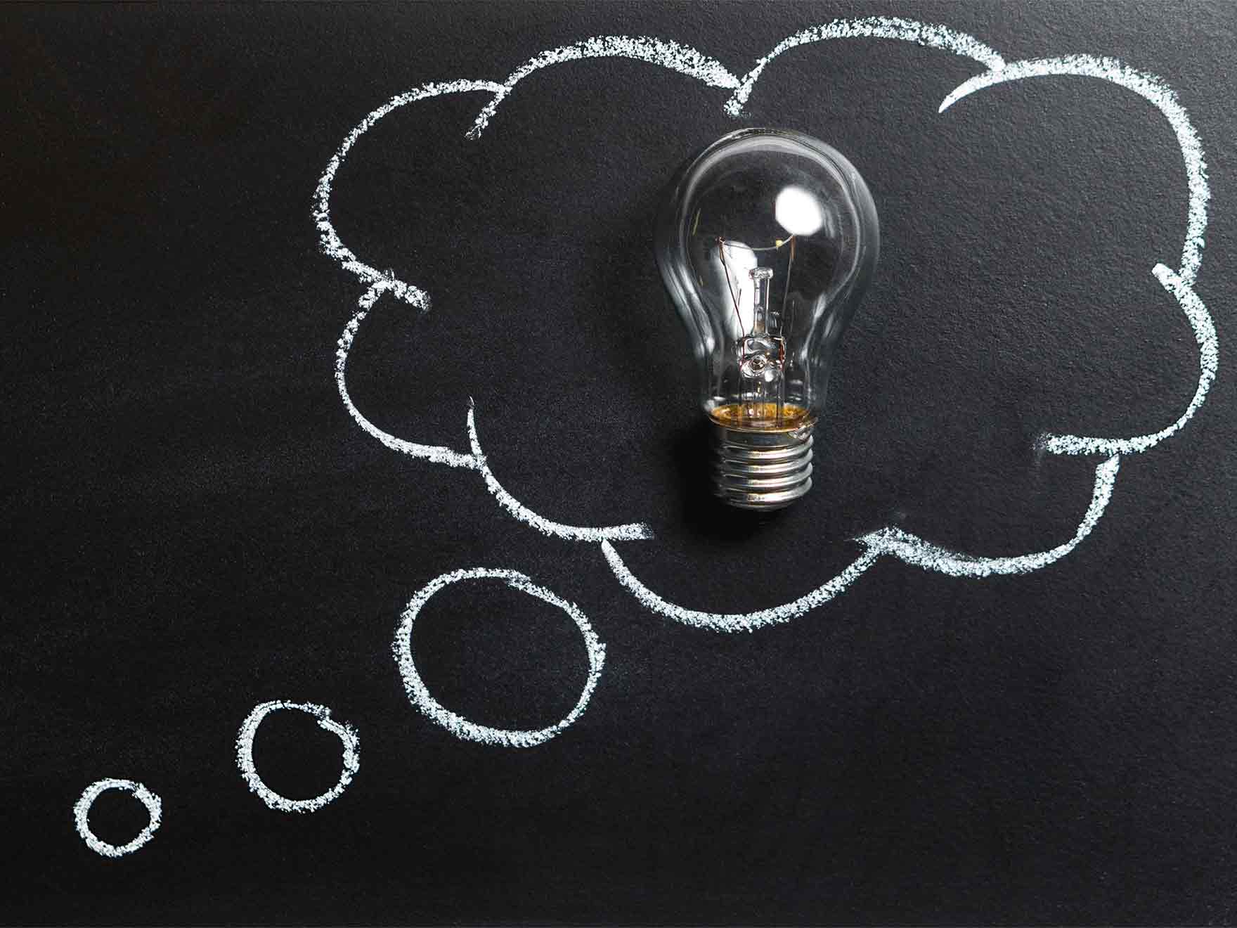 A lightbulb sits inside of a thought bubble drawn in chalk.