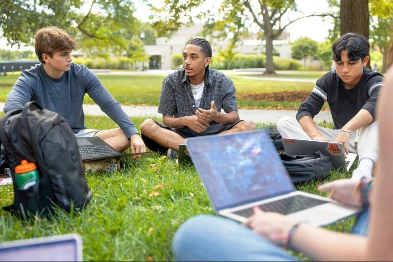 Students sit outside in the grass with their laptops for a Grand Challenges course.