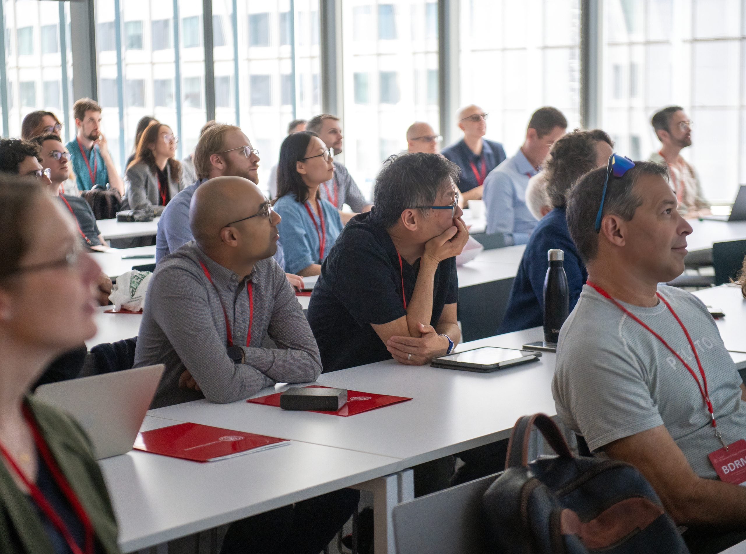 BDRM conference attendees sit and listen to a presentation with sunlight streaming in from a wall of windows.