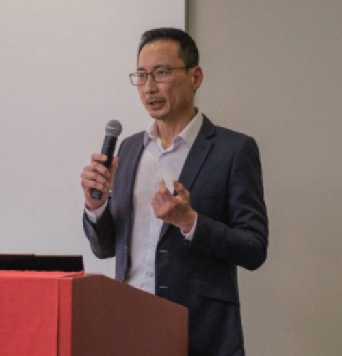 Geoffrey Lim, MBA '00, with a microphone, speaking at podium.