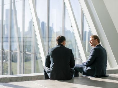 Two male business professionals talking with the NYC skyline in the back.