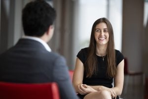A woman with long brown hair smiles at a man sitting across from her in the foreground.