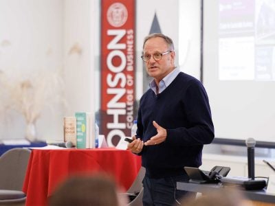 A man speaks to an audience in front of a Johnson School banner.