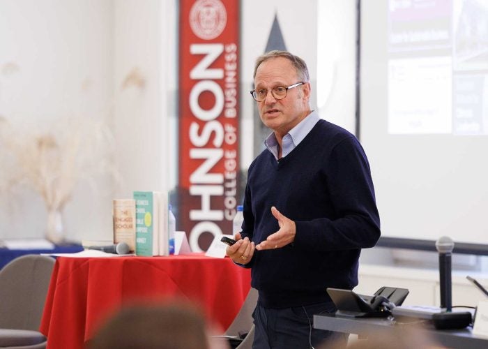 A man speaks to an audience in front of a Johnson School banner.