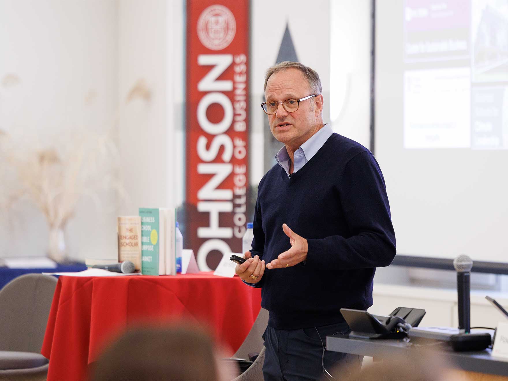 A man speaks to an audience in front of a Johnson School banner.