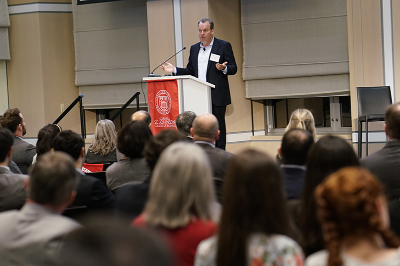 Photo of Alan Rosen speaking at a podium to a group of seated listeners