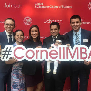 Photo of Carlos, Abby, and friends holding the #CornellMBA banner at orientation