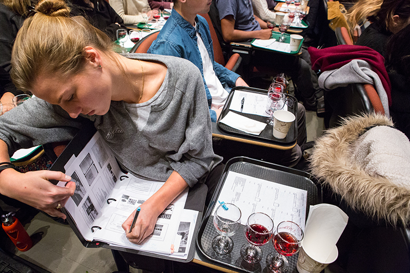 Photo of a student writing in her notebook with samples of wine nearby