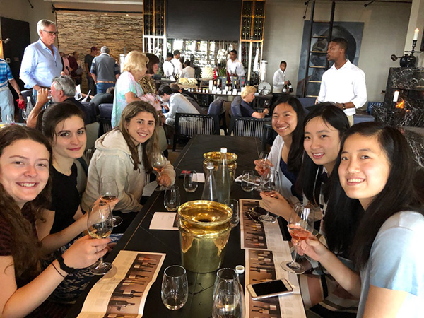 Photo of students sitting around a table with wine glasses and papers