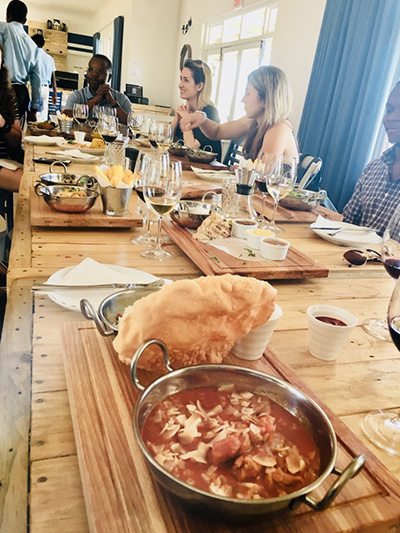 Photo of food on a large wooden table surrounded by students