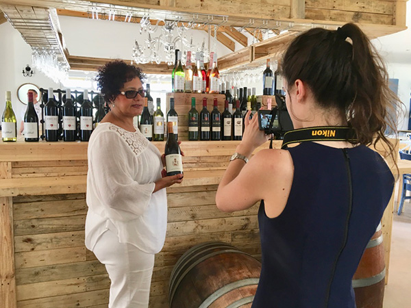 Photo of a student taking a video of Vivian holding a bottle of wine