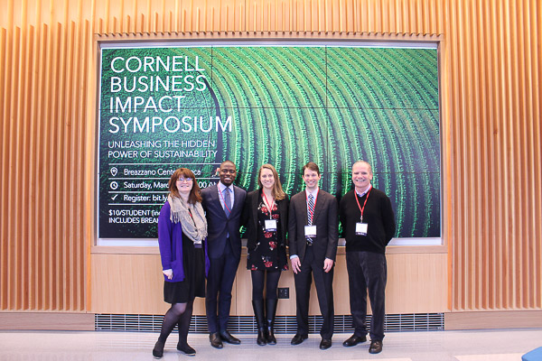 Photo of speakers standing in front of a screen that says Cornell Business Impact Symposium