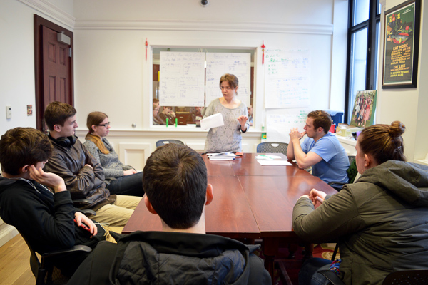Photo of six students sitting around a table with one teacher speaking to them