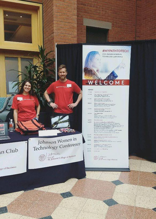 Photo of students standing behind a table with a Johnson Women in Technology banner