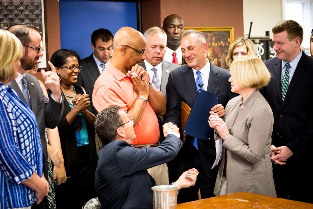 Photo of Gary shaking hands with the governor, surrounded by a room full of supporters