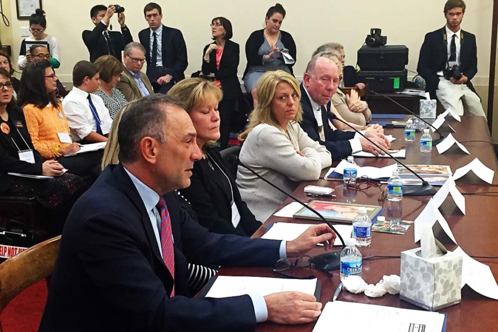 Photo of Mendell sitting at a desk among others speaking into a microphone