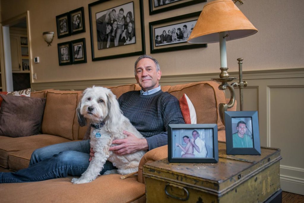 Photo of Mendell sitting on a couch with his dog and photos of his son