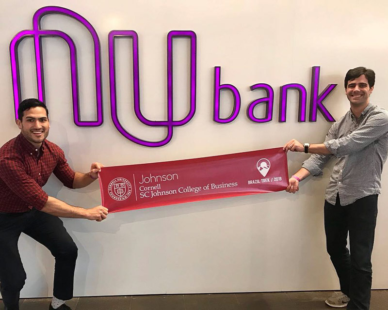 Photo of two students holding a Johnson banner under the Nubank logo