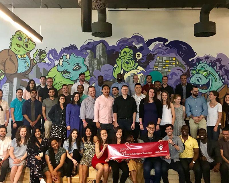Photo of students holding a Johnson banner with a colorful mural behind them