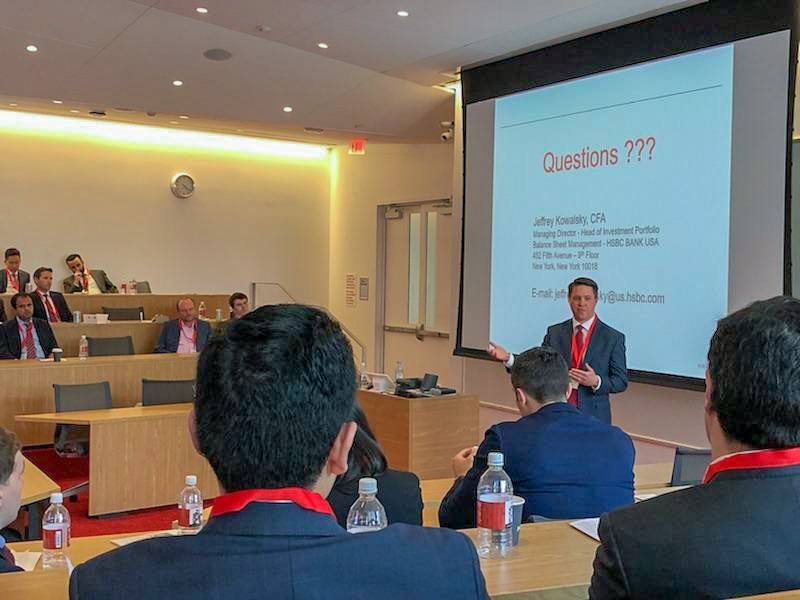 Photo of a man speaking to a lecture hall with a slide presentation