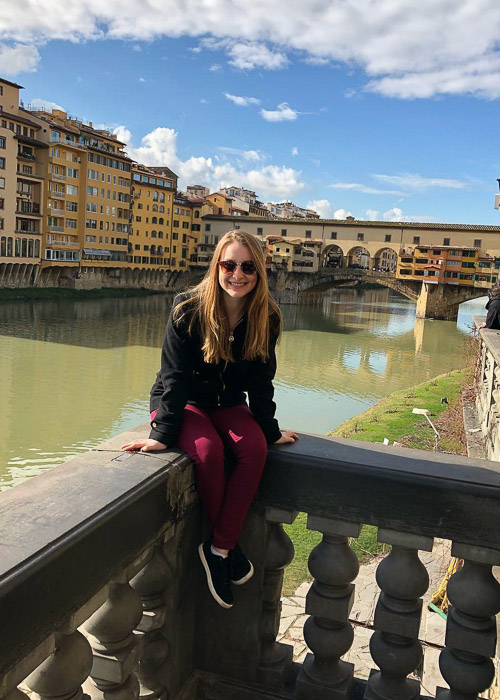 Photo of Rachel sitting on a railing overlooking a city and river