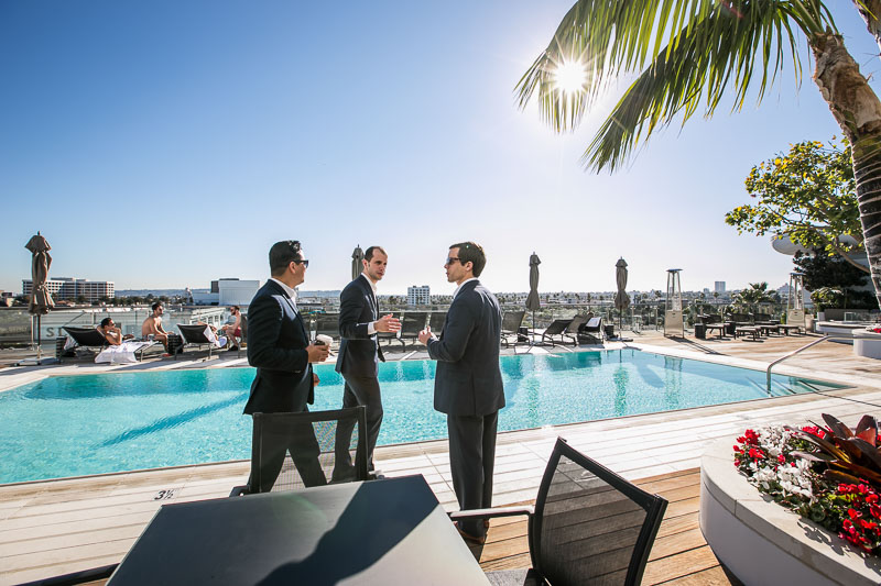 Photo of three men wearing suits and talking near a pool