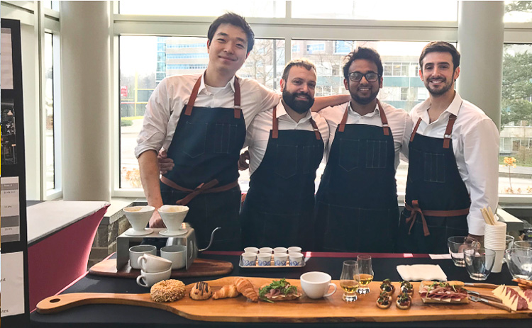 Photo of four students standing behind a table of food wearing aprons