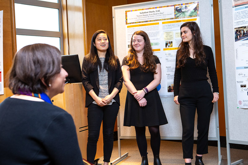 Photo of three female students presenting at the front of the room with posters