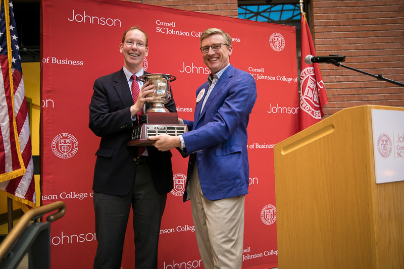 Photo of Dean Nelson presenting a large trophy/cup to a gentleman at a podium