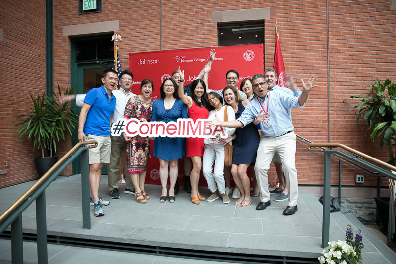 Photo of group of attendees on stage holding a #CornellMBA sign