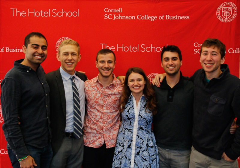 A group of ambassadors standing in front of a Hotel School banner