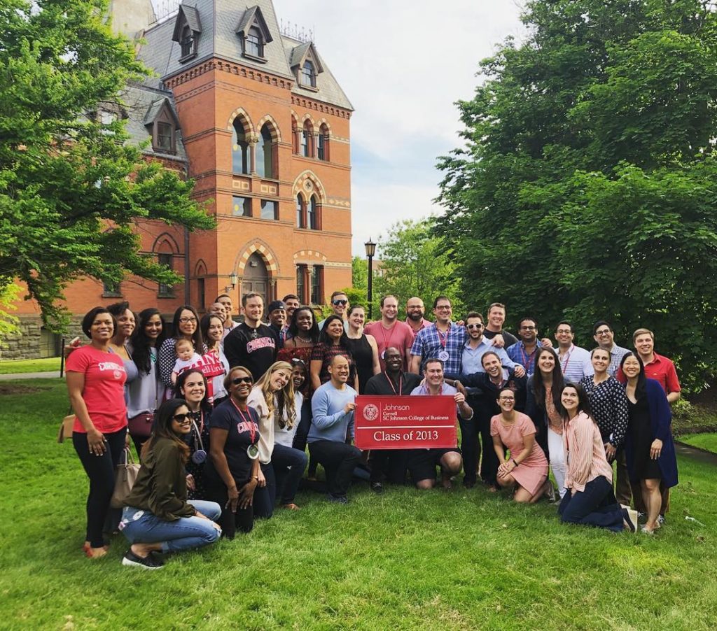 Large group of Reunion attendees holding a banner outside Sage Hall