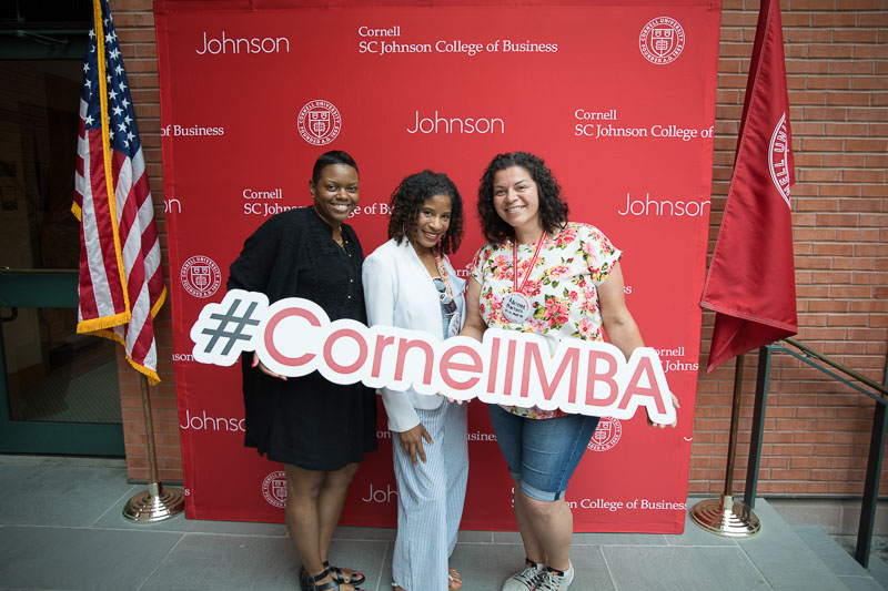 Photo of three women holding the #CornellMBA banner