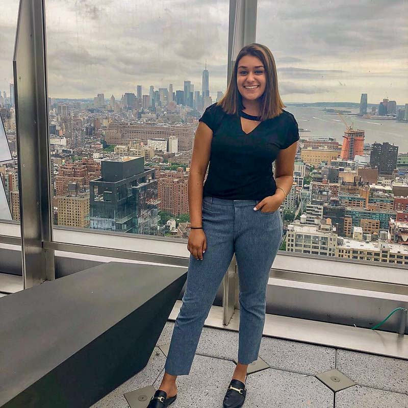 Photo of Aditi in a high rise building with the city in the window behind her