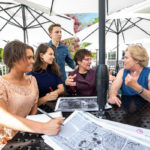 Photo of four students and Reneta sitting around a patio table with blueprints