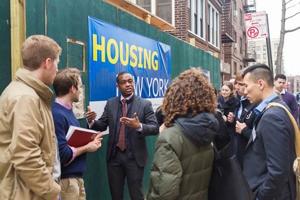 Photo of students standing with a speaker outside next to a Housing NYC sign