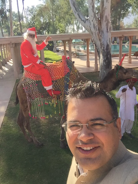 Photo of a Prateek taking a selfie with a camel in the background; Santa is sitting on the camel